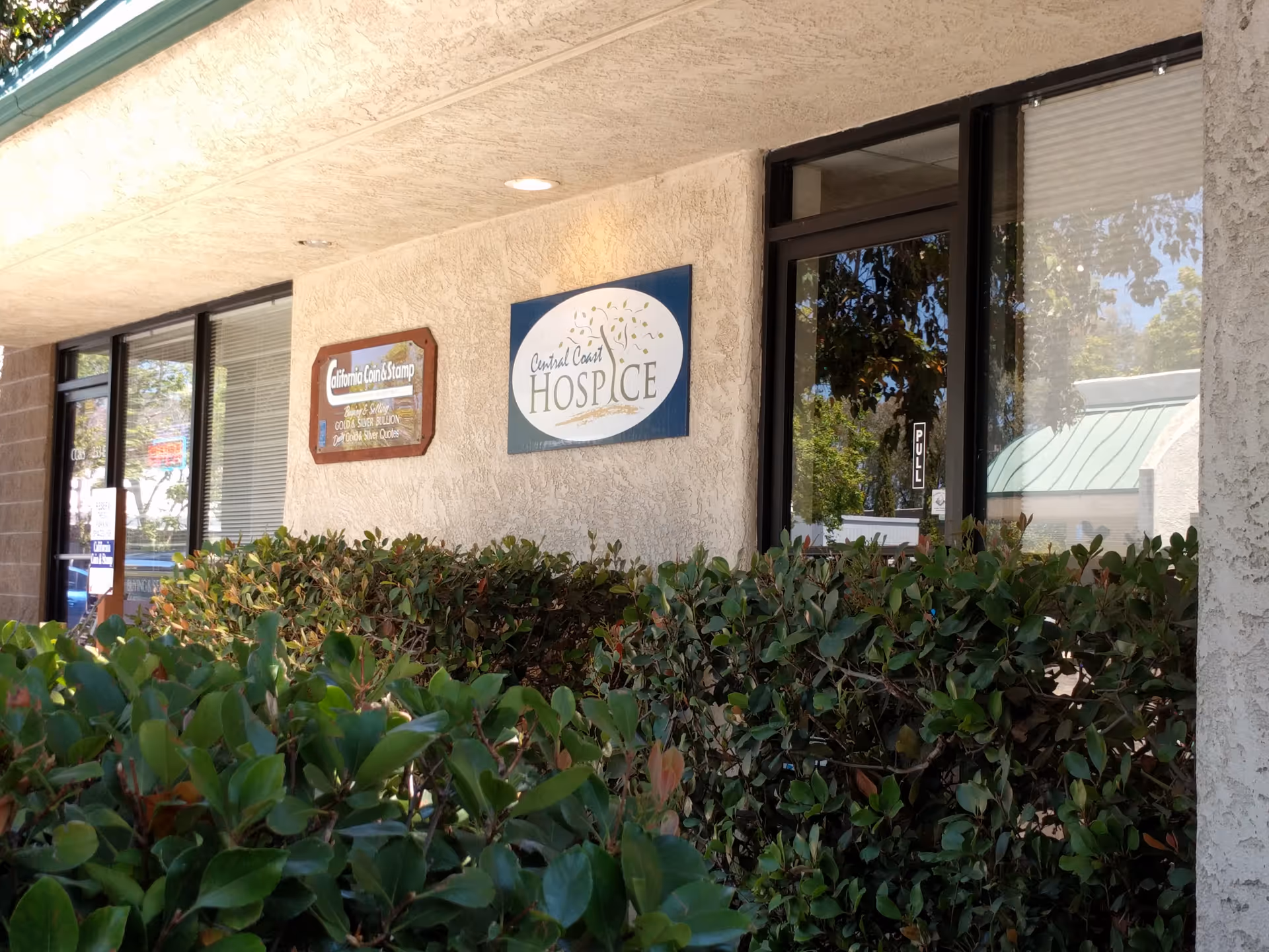 Exterior view of Central Coast Hospice facility with shrubs and signs along the front wall.