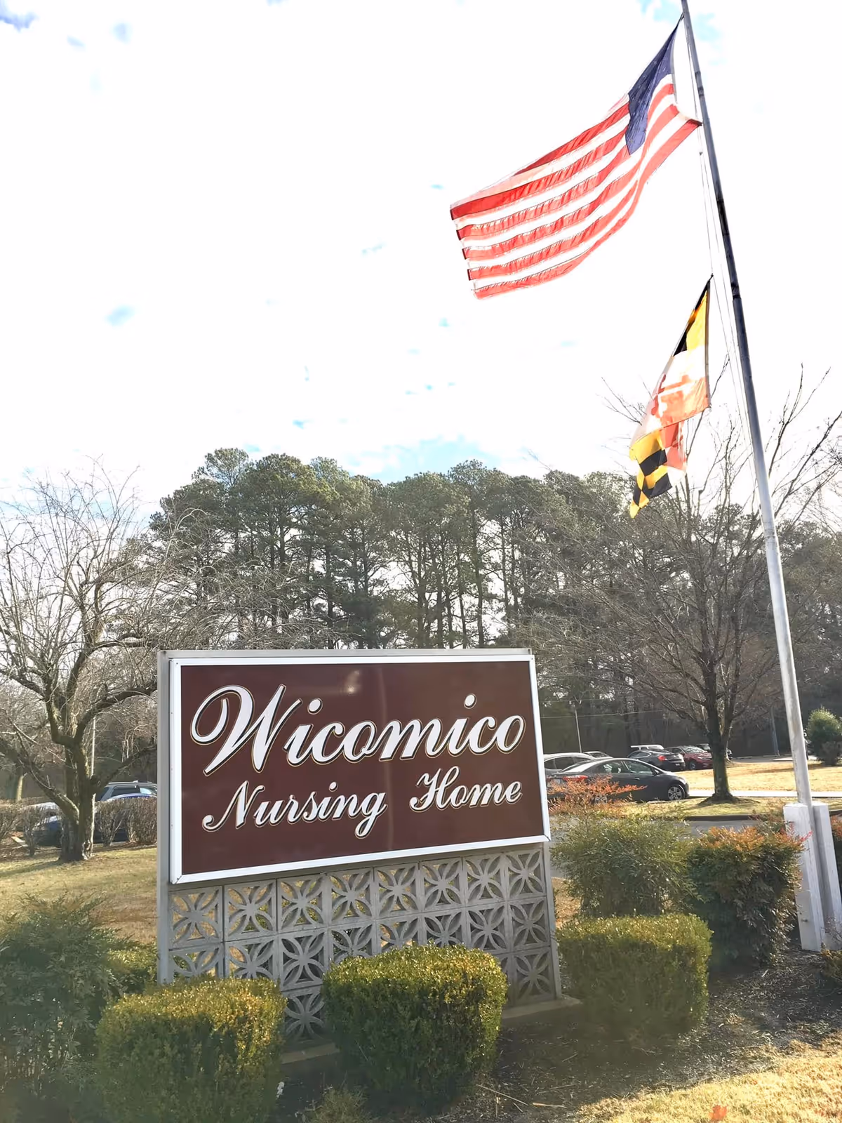 Exterior view of Wicomico Nursing Home sign, flagpoles, and neatly trimmed shrubs.