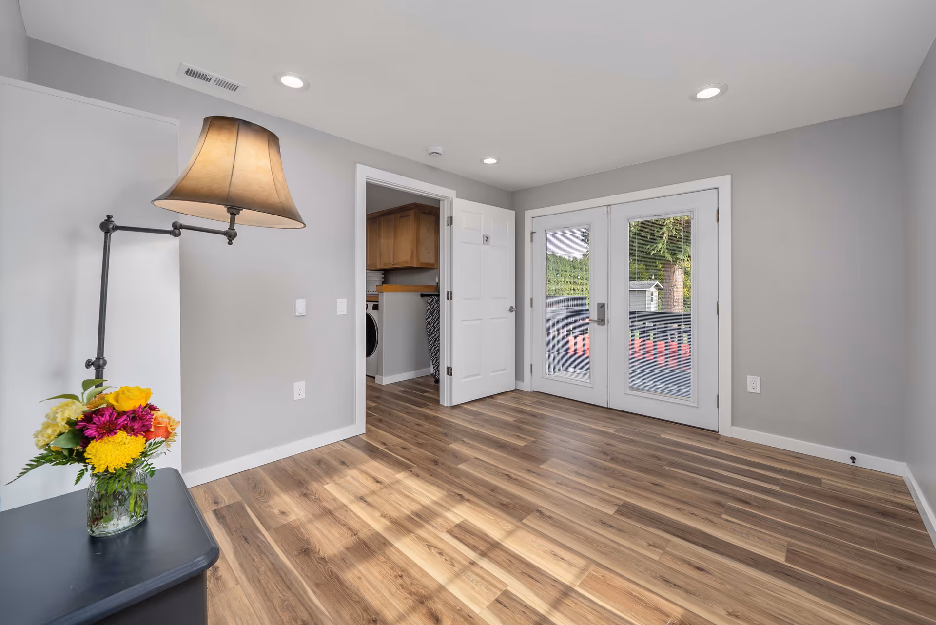 Bright, modern interior room with wooden floor, glass doors, and a vase of flowers.
