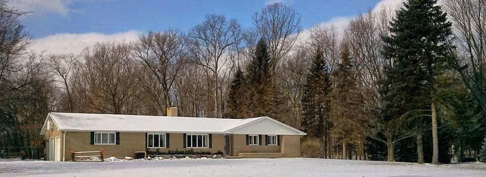 Single-story ranch-style building with a snow-covered lawn and leafless trees in the background under a partly cloudy sky.