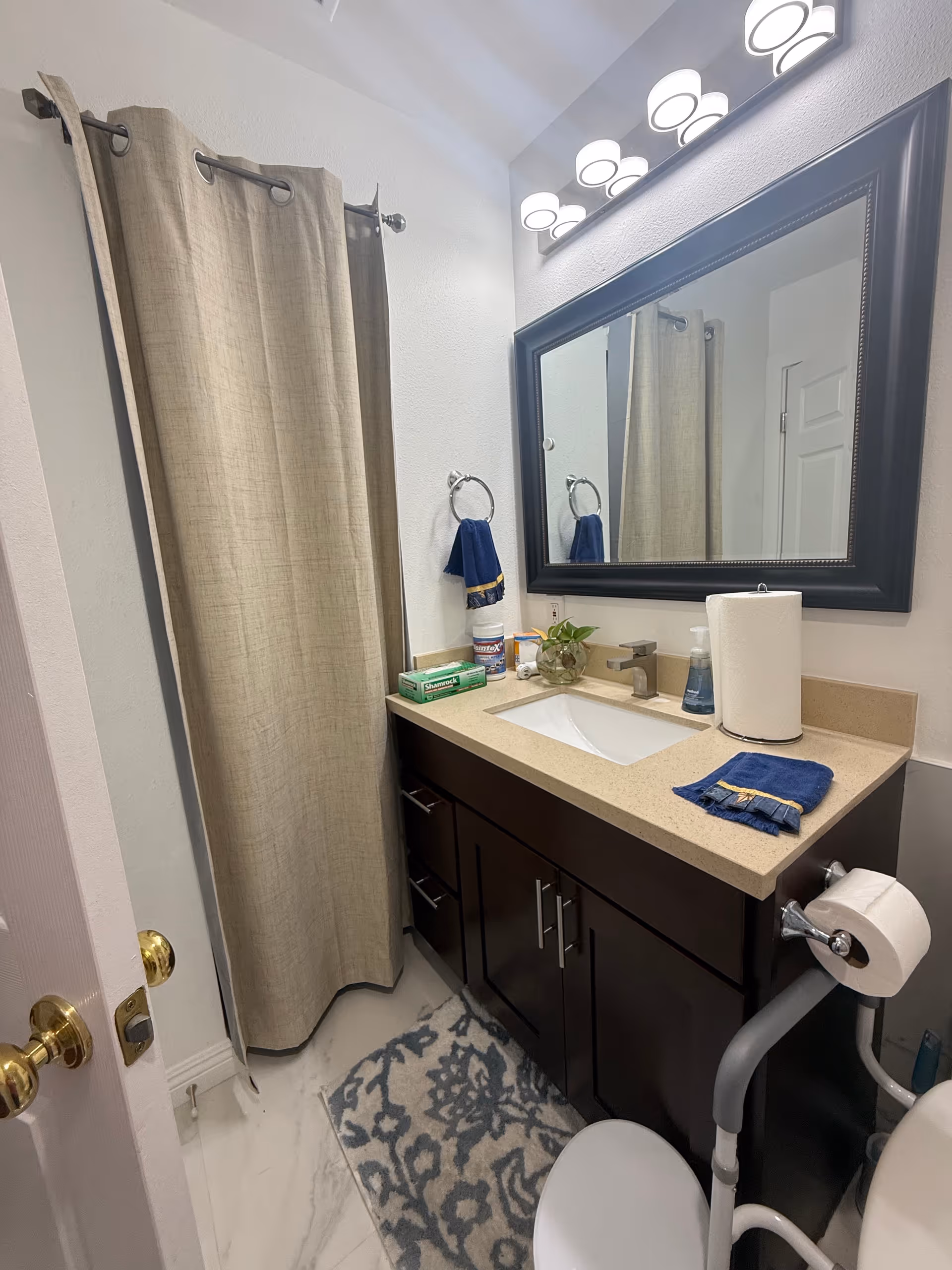 Bathroom with beige shower curtain, dark vanity, framed mirror, and countertop items.