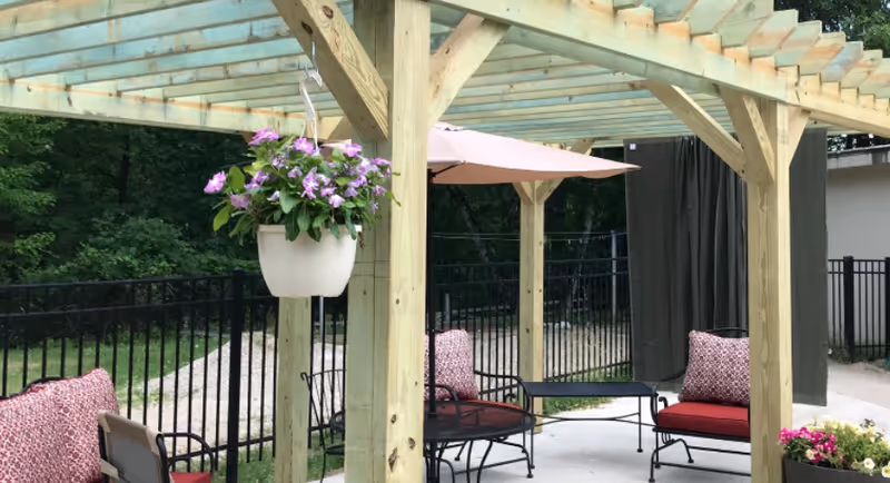 Wooden pergola over a paved outdoor seating area with cushions and hanging flowers.