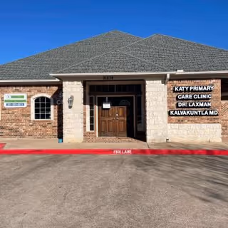 Front exterior of a brick clinic building with wooden door and Katy Primary Care Clinic signage.