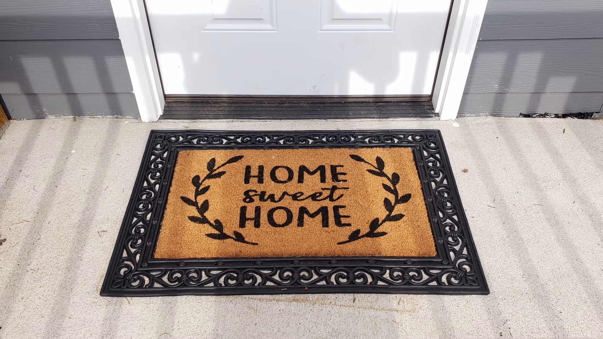 Brown welcome mat reading Home Sweet Home sits before a white front door.