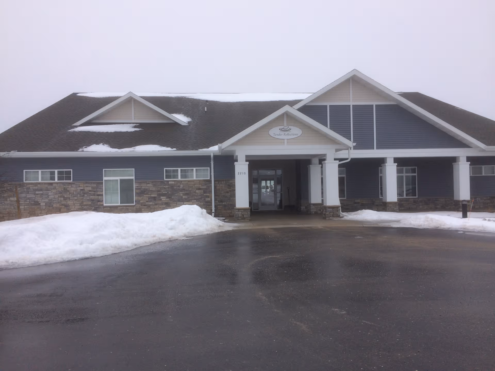 Front entrance of a modern assisted living facility with a covered entry and snow.