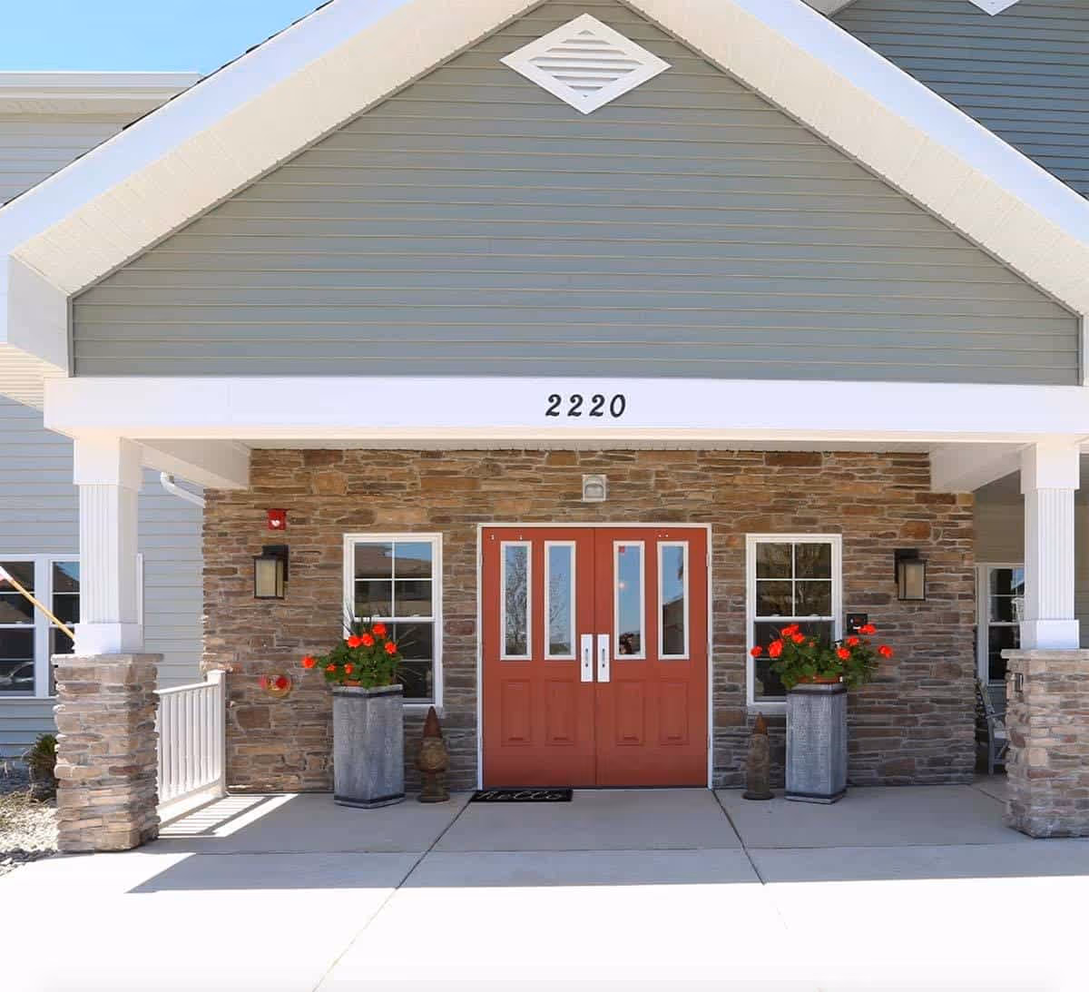 Front entrance of Milestone Senior Living Stoughton with red doors and stone facade.