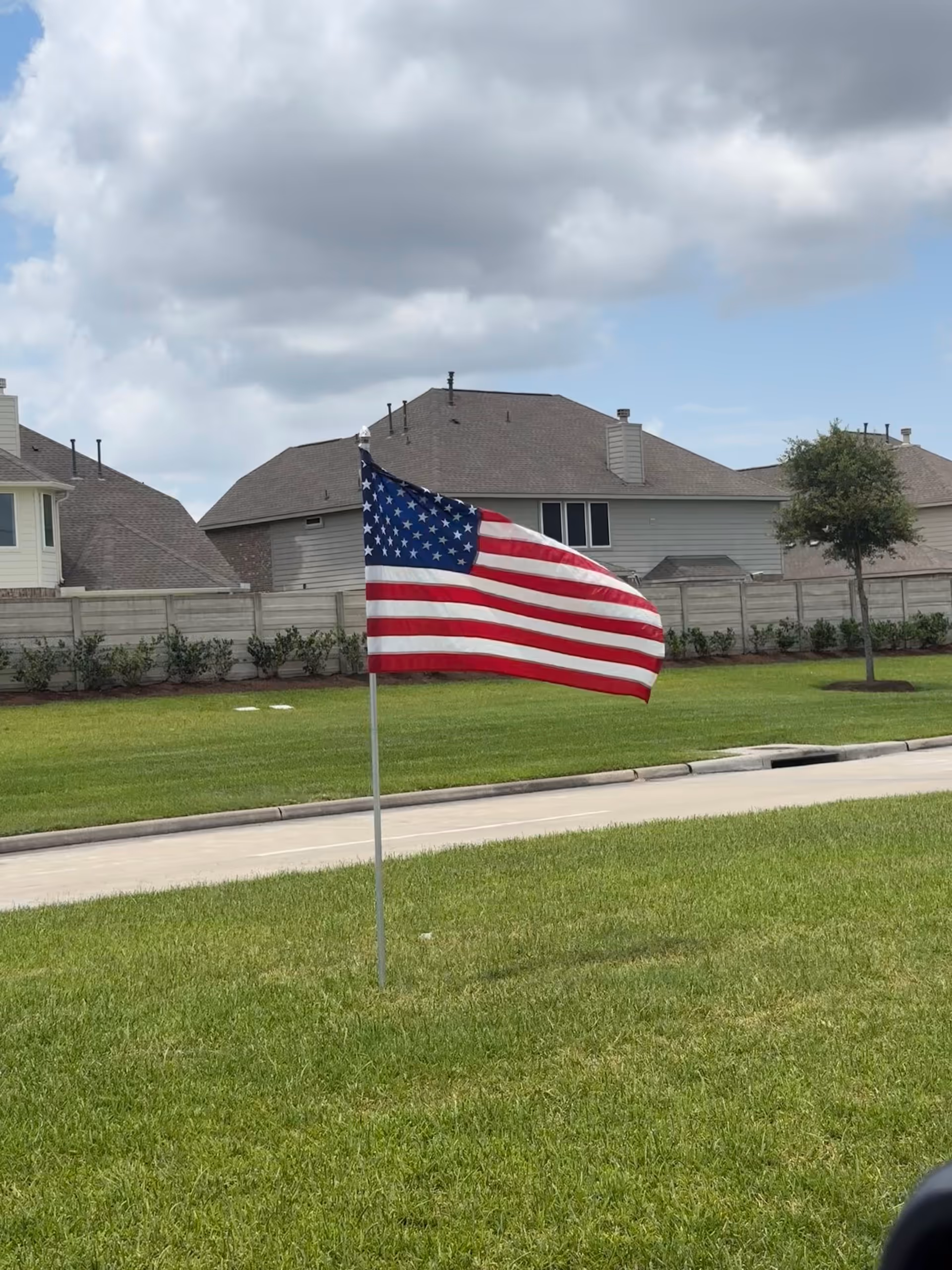 American flag on a flagpole in a green lawn with houses in the background