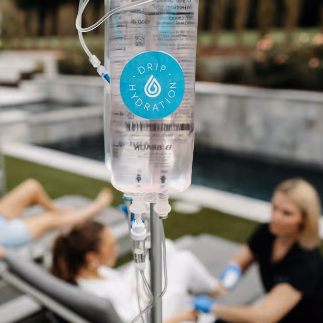 IV drip bag labeled Drip Hydration near poolside with lounging patients.