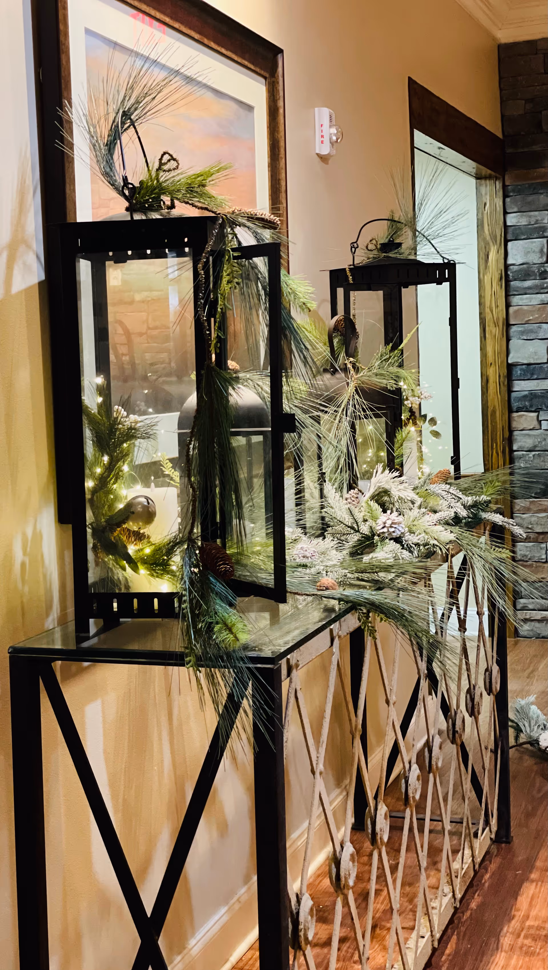 Decorative lanterns with pine garlands sit on a glass-topped console along a hallway.