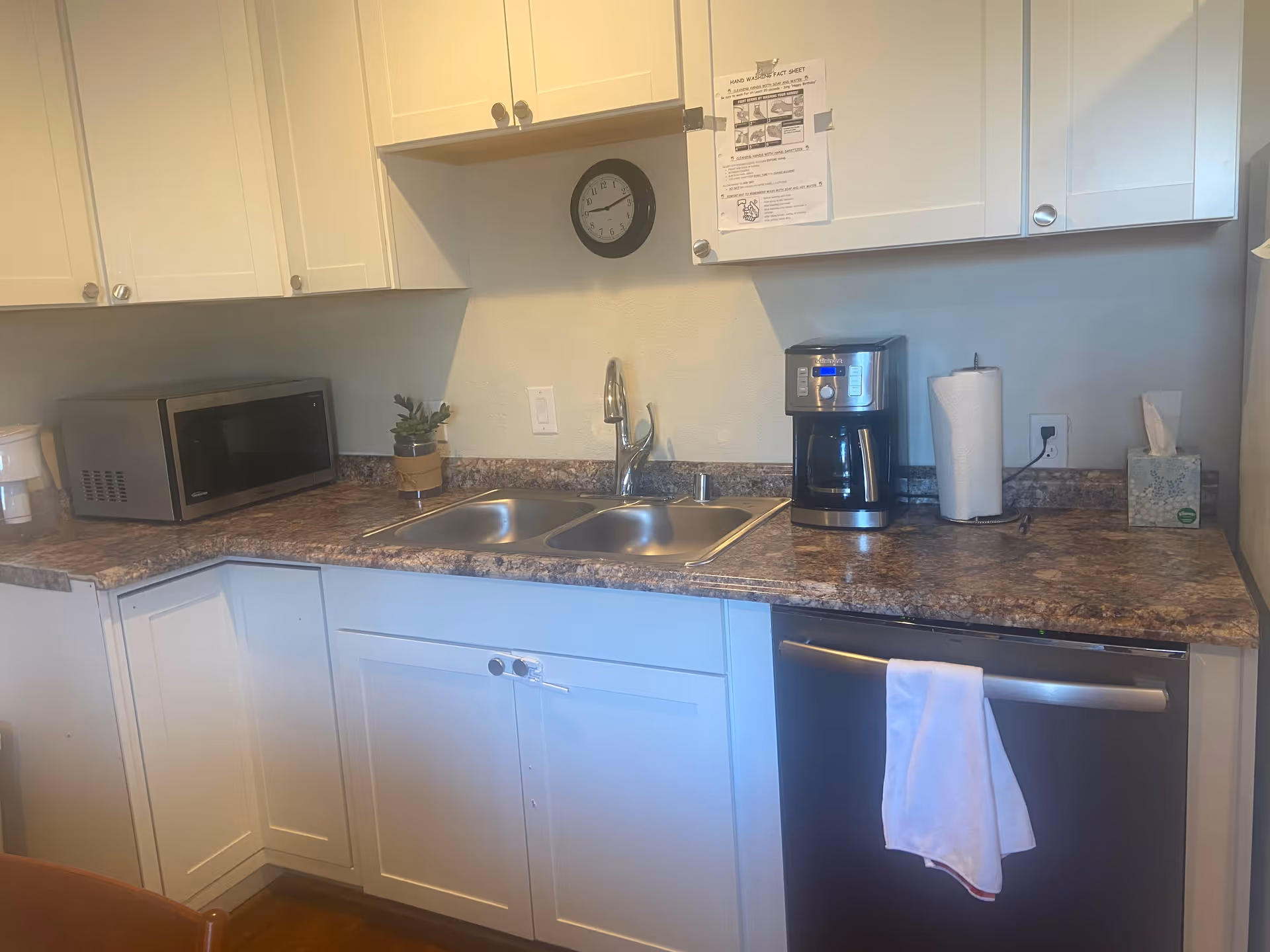 Senior living kitchen with sink, microwave, coffee maker, dishwasher, and white cabinets.