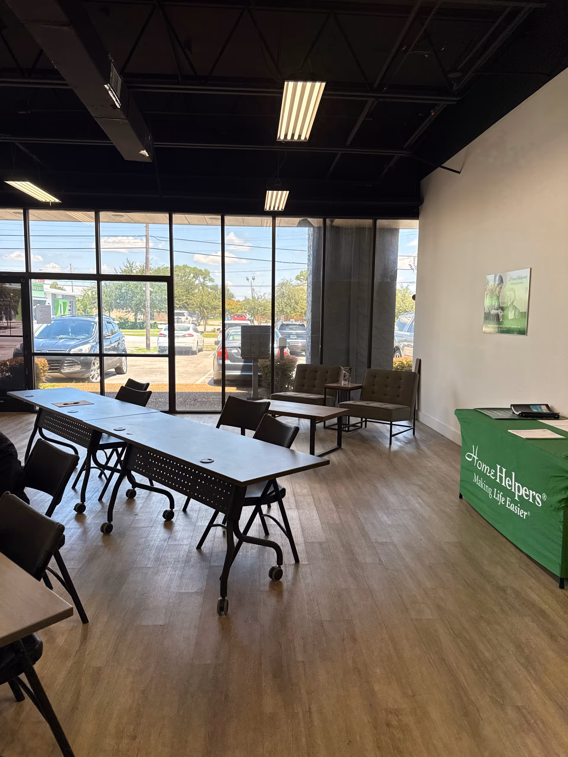 Indoor community room with long tables, chairs, large windows, and a Home Helpers banner.