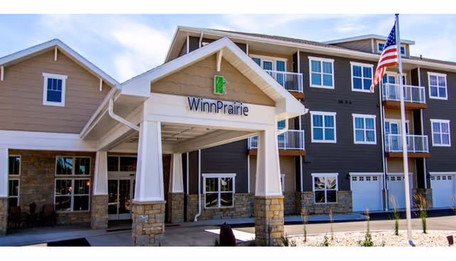 Exterior view of WinnPrairie senior living building with entrance canopy and American flag.