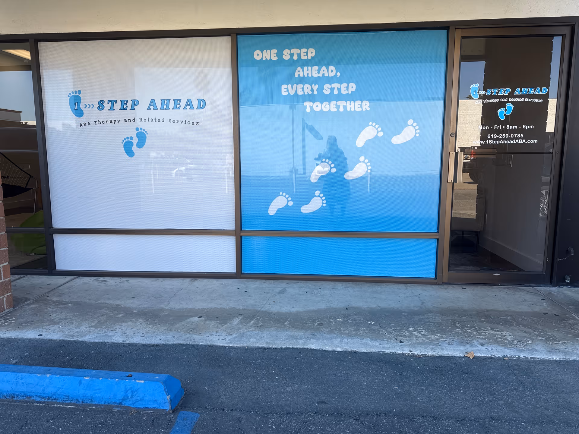 Exterior storefront signage for One Step Ahead ABA with blue panels and footprints