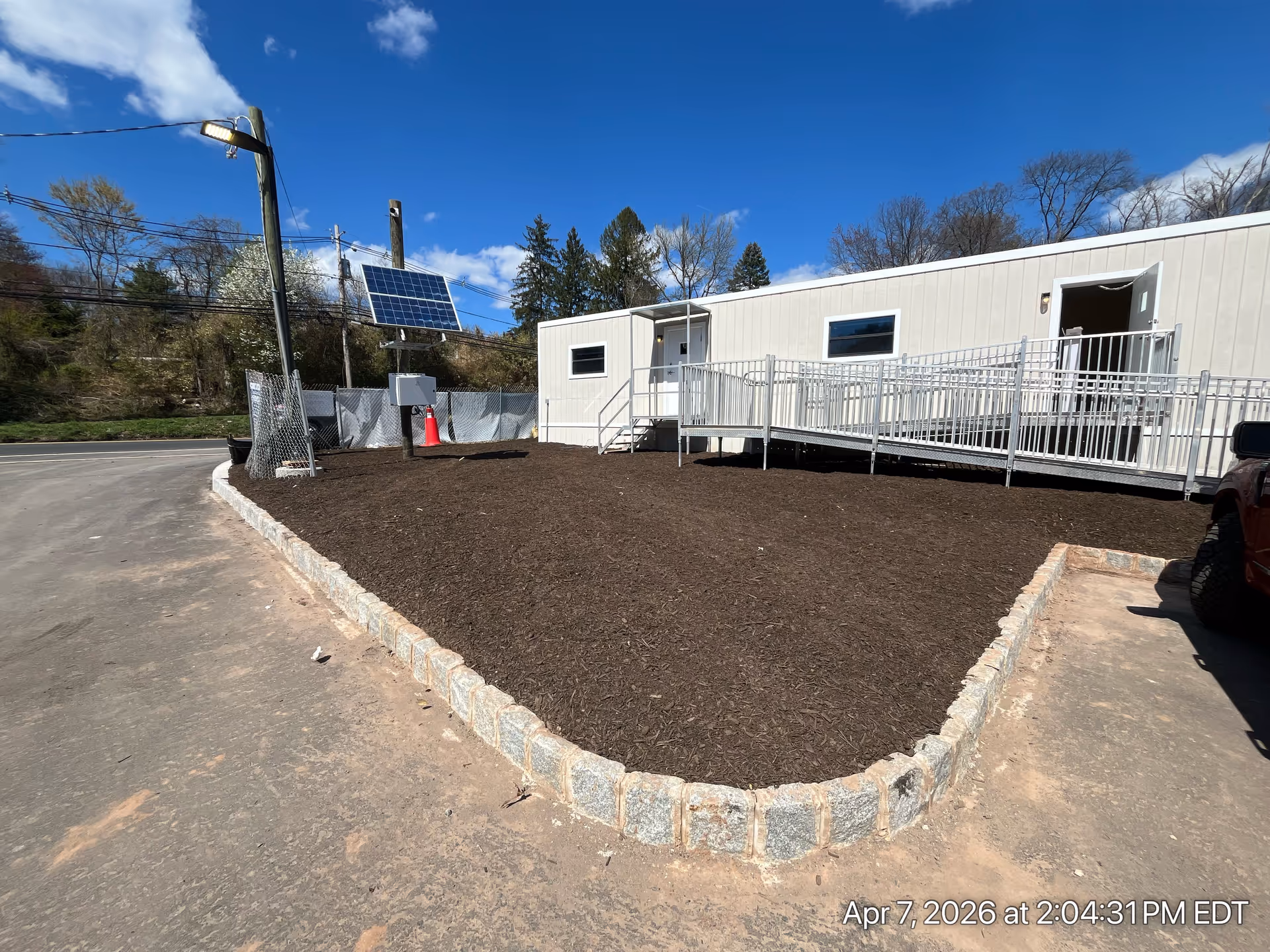 Exterior view of a beige modular building with ramp, mulch bed, and solar equipment.