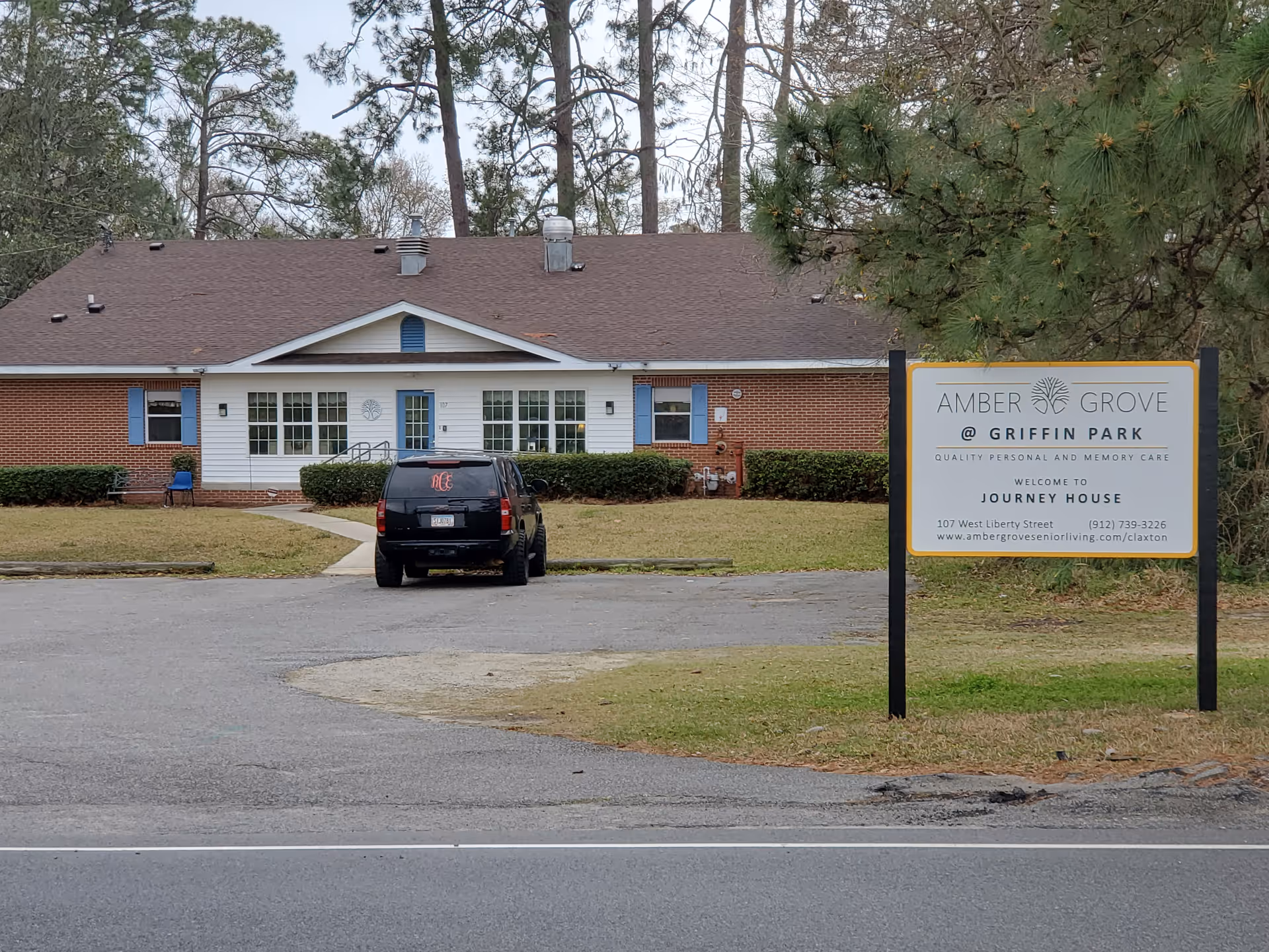Front view of a single-story senior living facility with a sign and parked car.