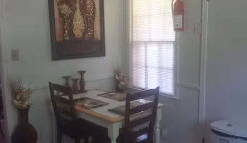 A small dining nook with a table, two chairs, wall art, and window blinds.