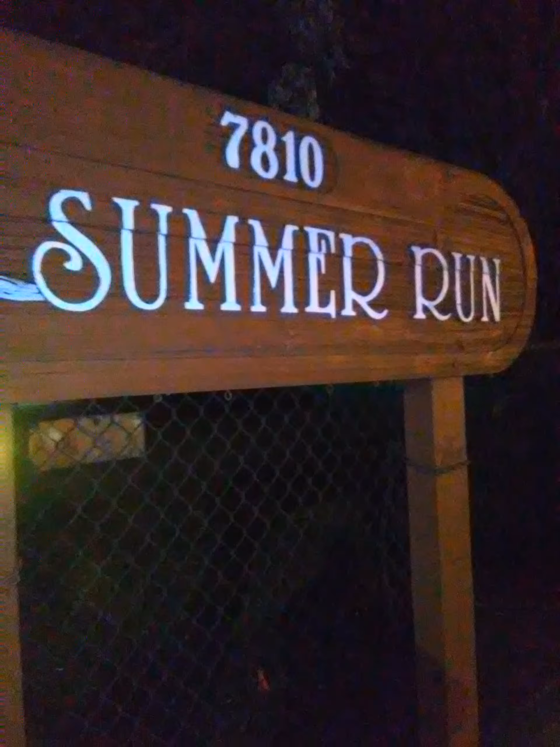Night shot of a wooden sign reading '7810 Summer Run' in front of a facility.