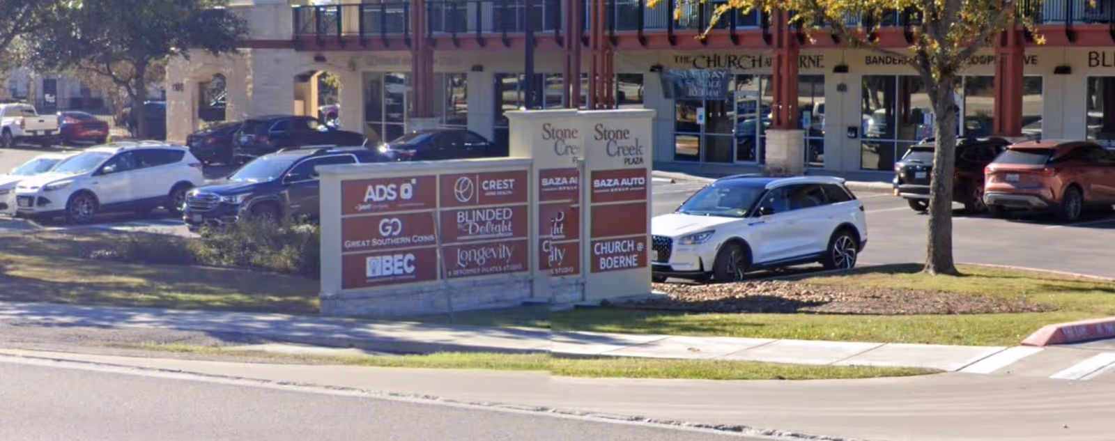 Exterior of a strip mall with parked cars and a central signboard.