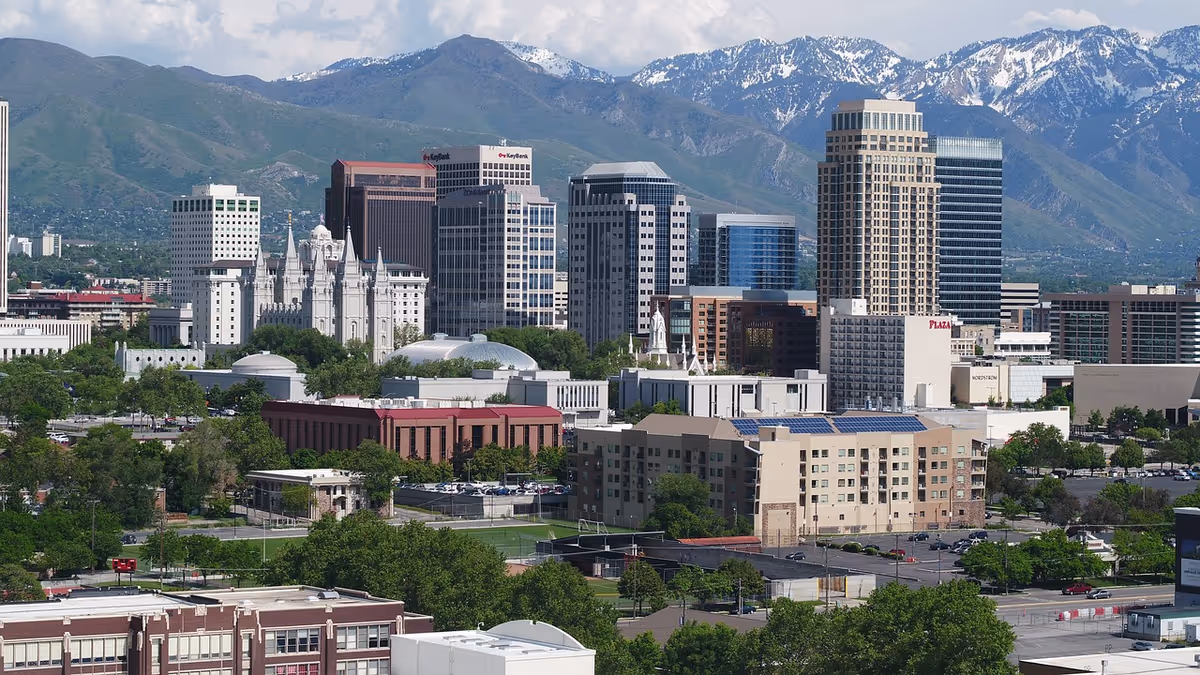 City skyline with tall buildings and distant snow-capped mountains under blue sky.
