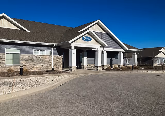 Single-story assisted living building with a covered main entrance, columns and a circular drive under a clear blue sky.
