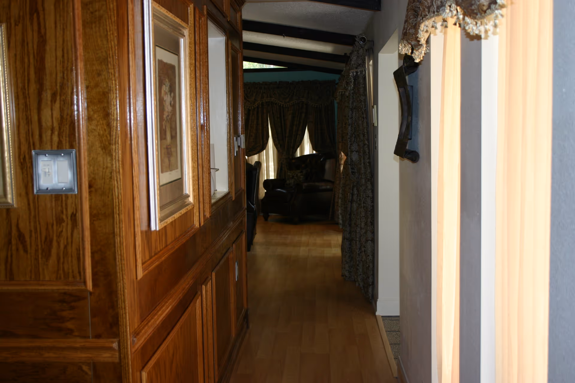 Narrow wooden hallway inside a senior living facility, leading to a distant living room.