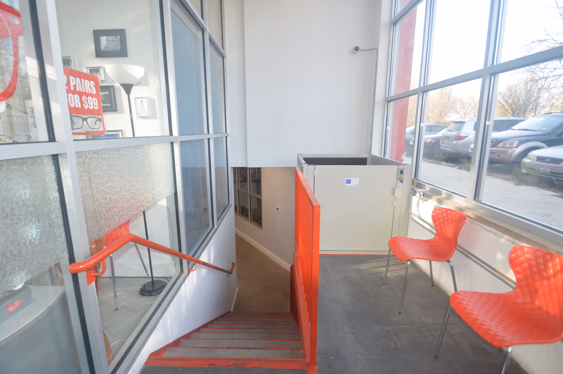 An indoor stairwell and lobby with red chairs beside large windows.