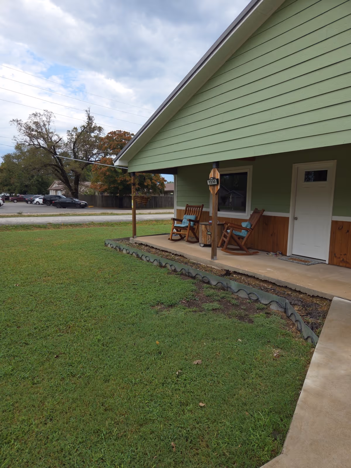 Exterior of a green Oswego Operator facility with a small porch, rocking chairs, and lawn.