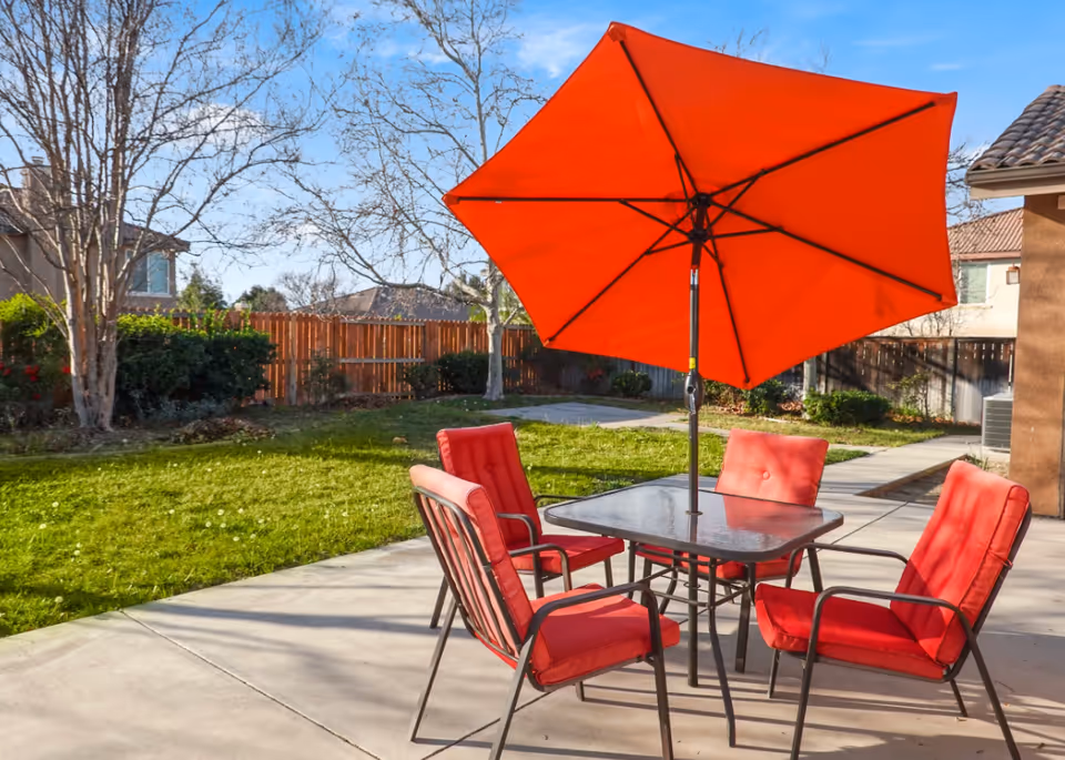 Red cushioned outdoor chairs surround a metal table beneath a large orange umbrella.