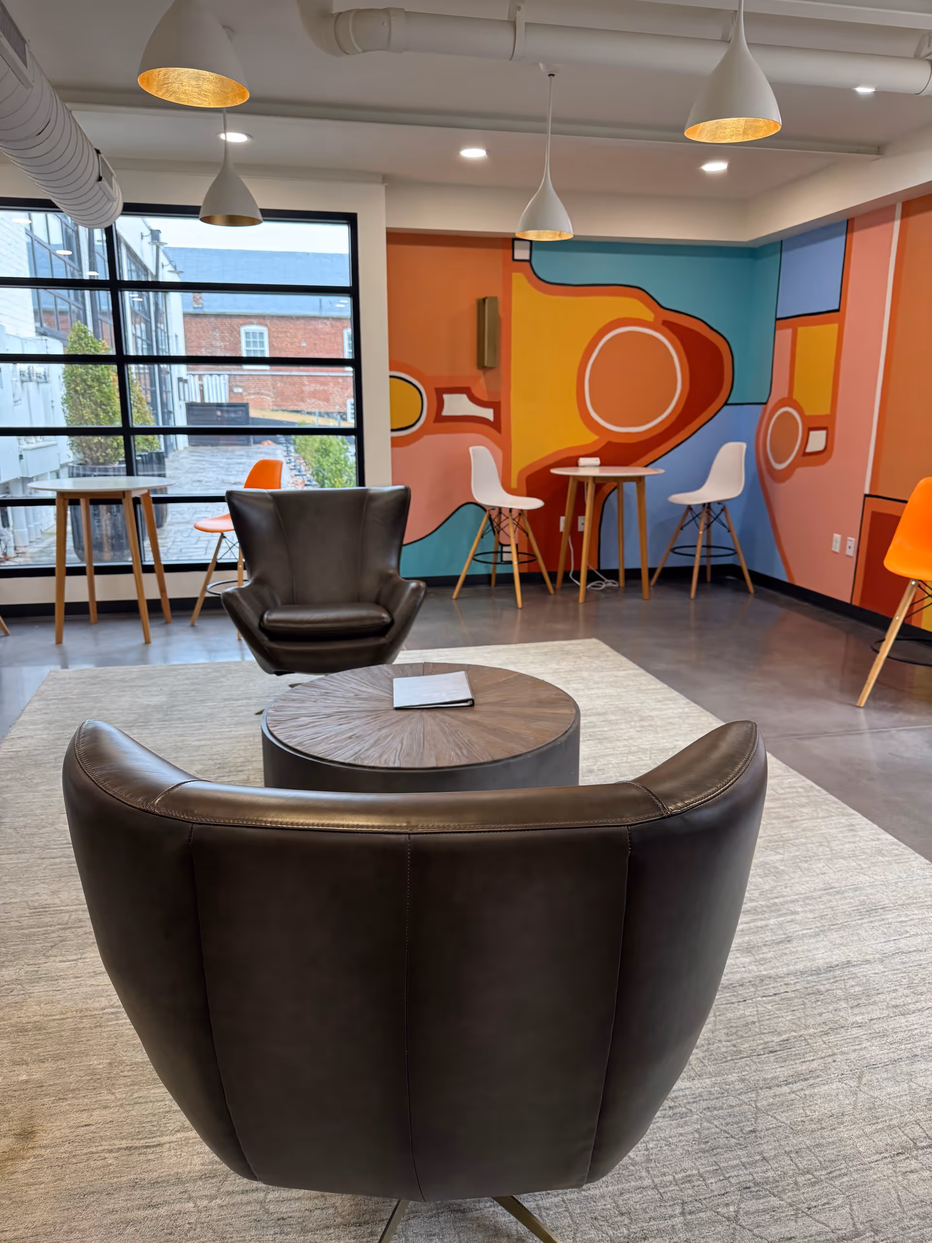 Modern lounge with leather chairs, round table, and colorful wall mural.
