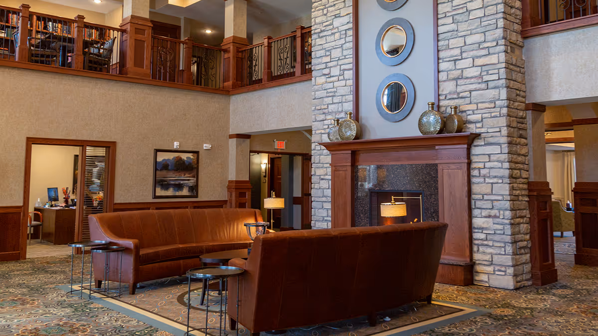 Interior senior living lounge with leather couches, a stone fireplace, and circular wall mirrors.