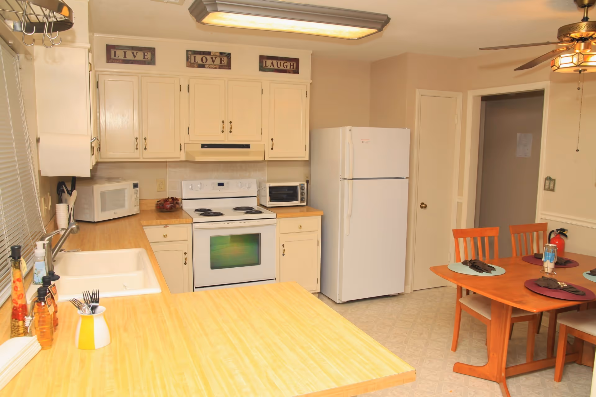 Bright kitchen area with white cabinets, stove, fridge, microwave, and a dining table.