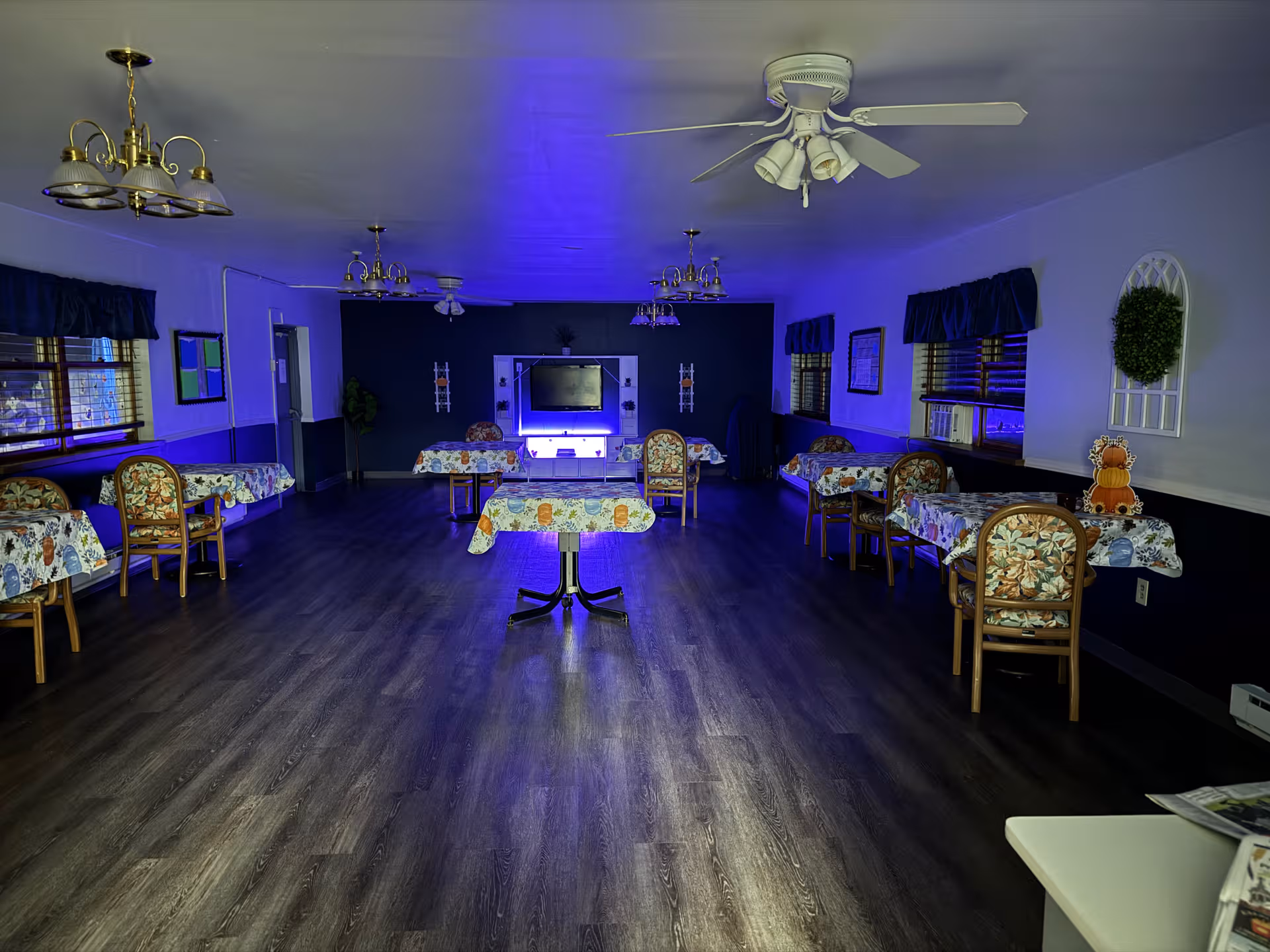 Spacious senior living dining room with floral tables and blue ambient lighting.