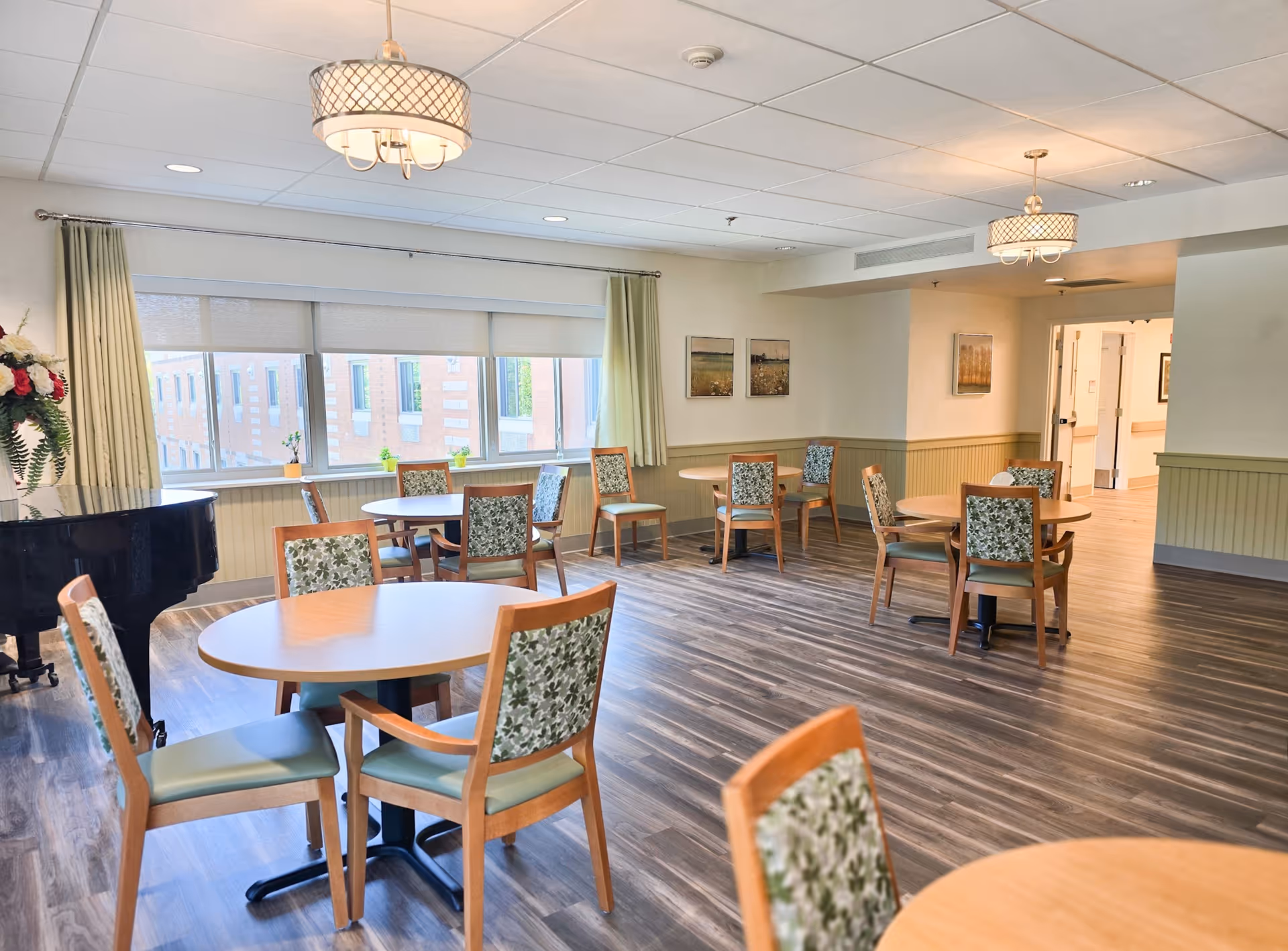 Bright dining lounge in a senior facility with round tables and patterned chairs.