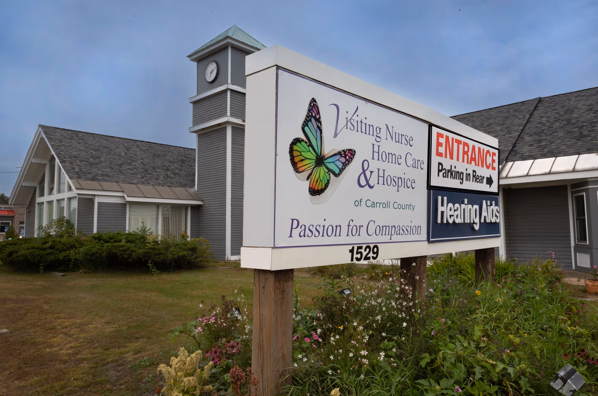 Exterior of Visiting Nurse Home Care & Hospice facility with large sign and garden beds.