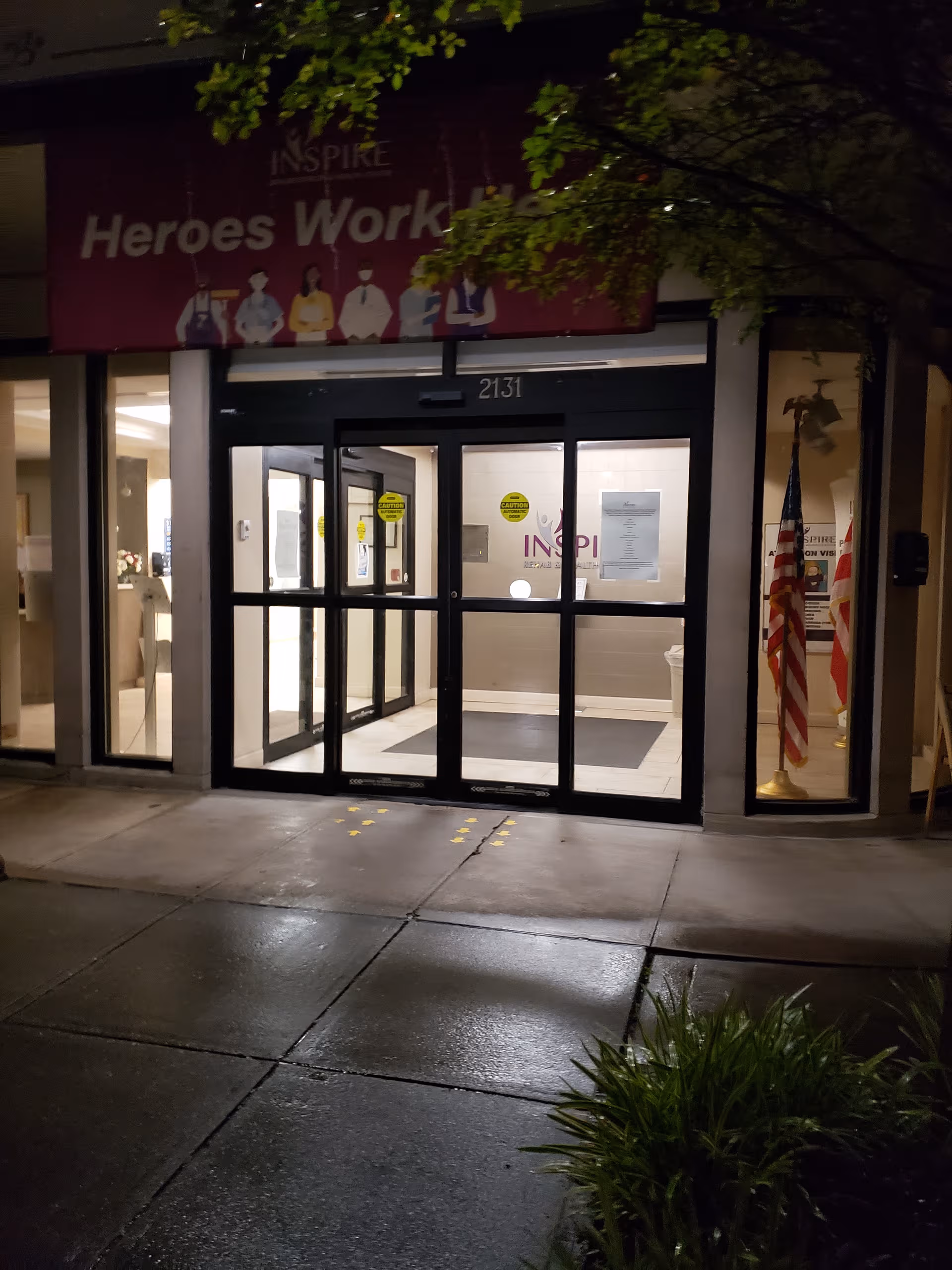 Night view of the glass-front entrance to Inspire Rehabilitation & Health Center with an American flag