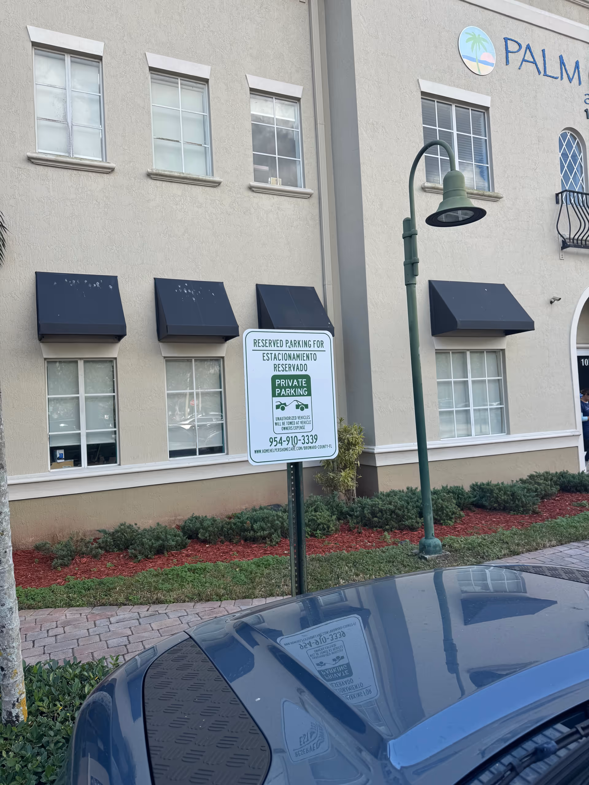 Exterior view of a beige senior living facility with dark awnings, parking sign, and landscaping.