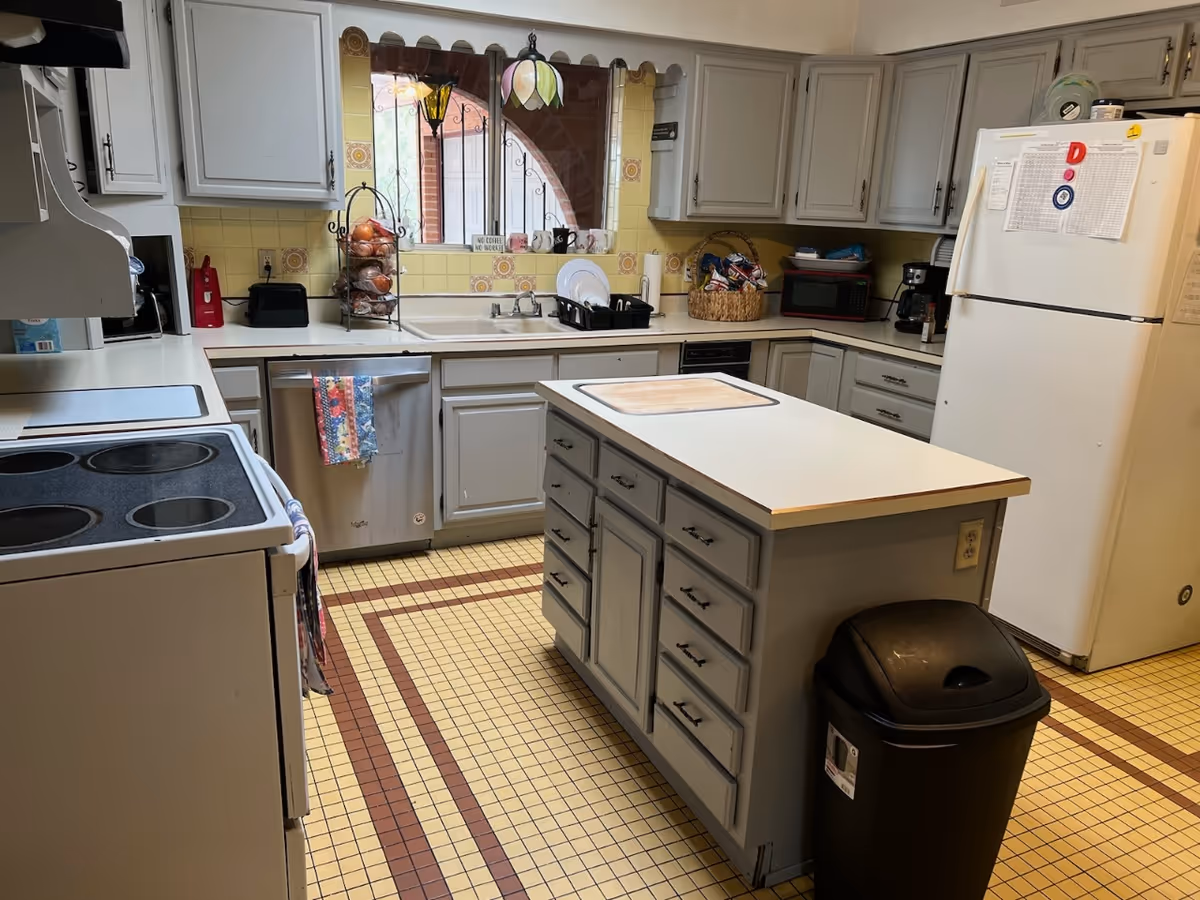 Grey kitchen with island, appliances, and a window behind the sink in a senior living facility.