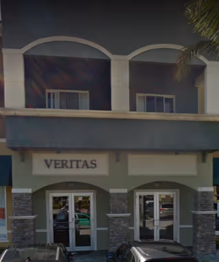 Veritas building entrance with arched windows, stone columns, and parked cars.
