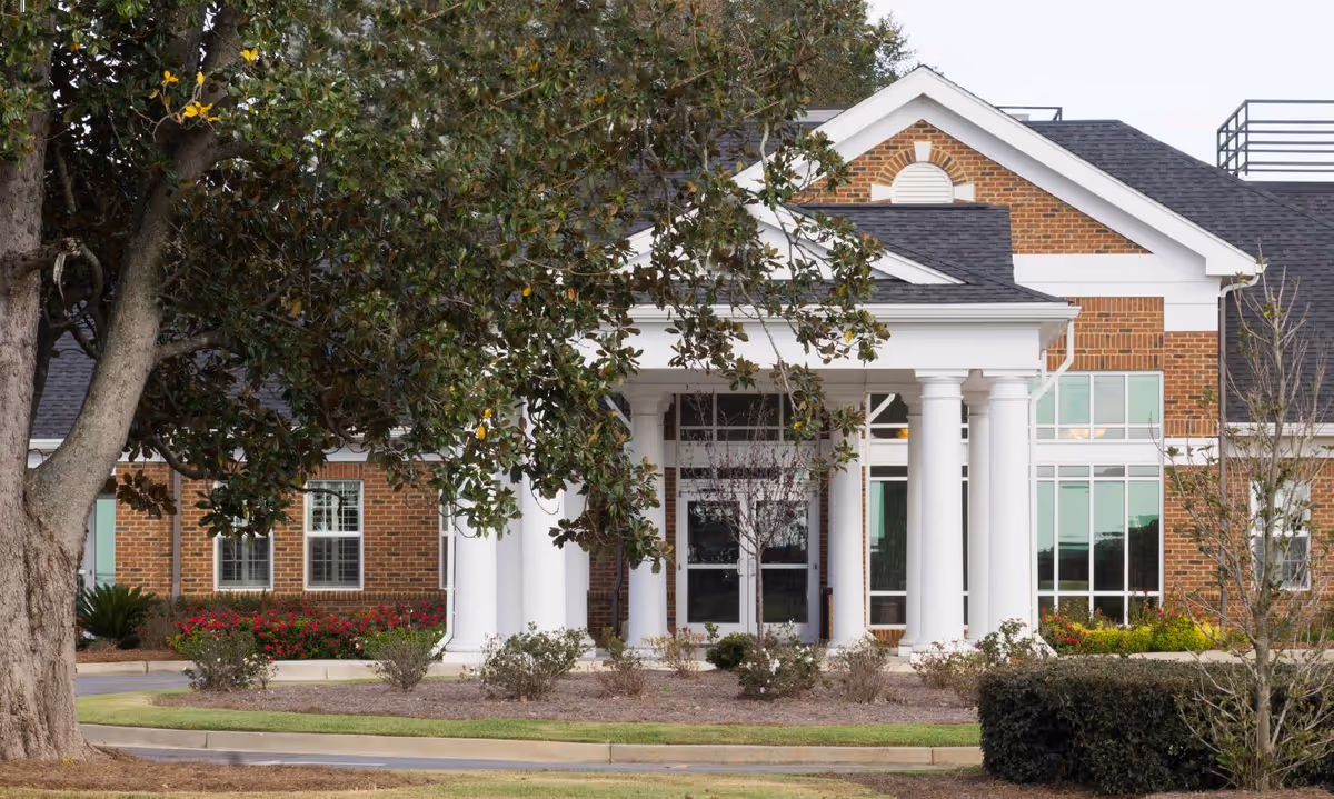 Front entrance of a brick senior living facility with white columns, large windows, and landscaped grounds.