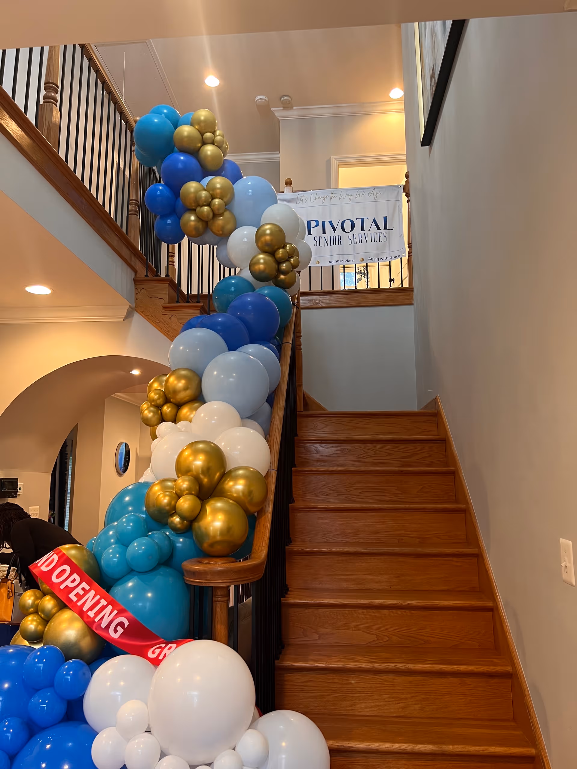 Indoor staircase adorned with blue, white, and gold balloons and a banner for Pivotal Senior Services.