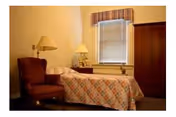 A bedroom in a senior residence featuring a bed, lamps, a window, and an armoire.