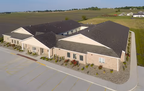 A single-story beige brick memory care facility with multiple connected wings and parking.