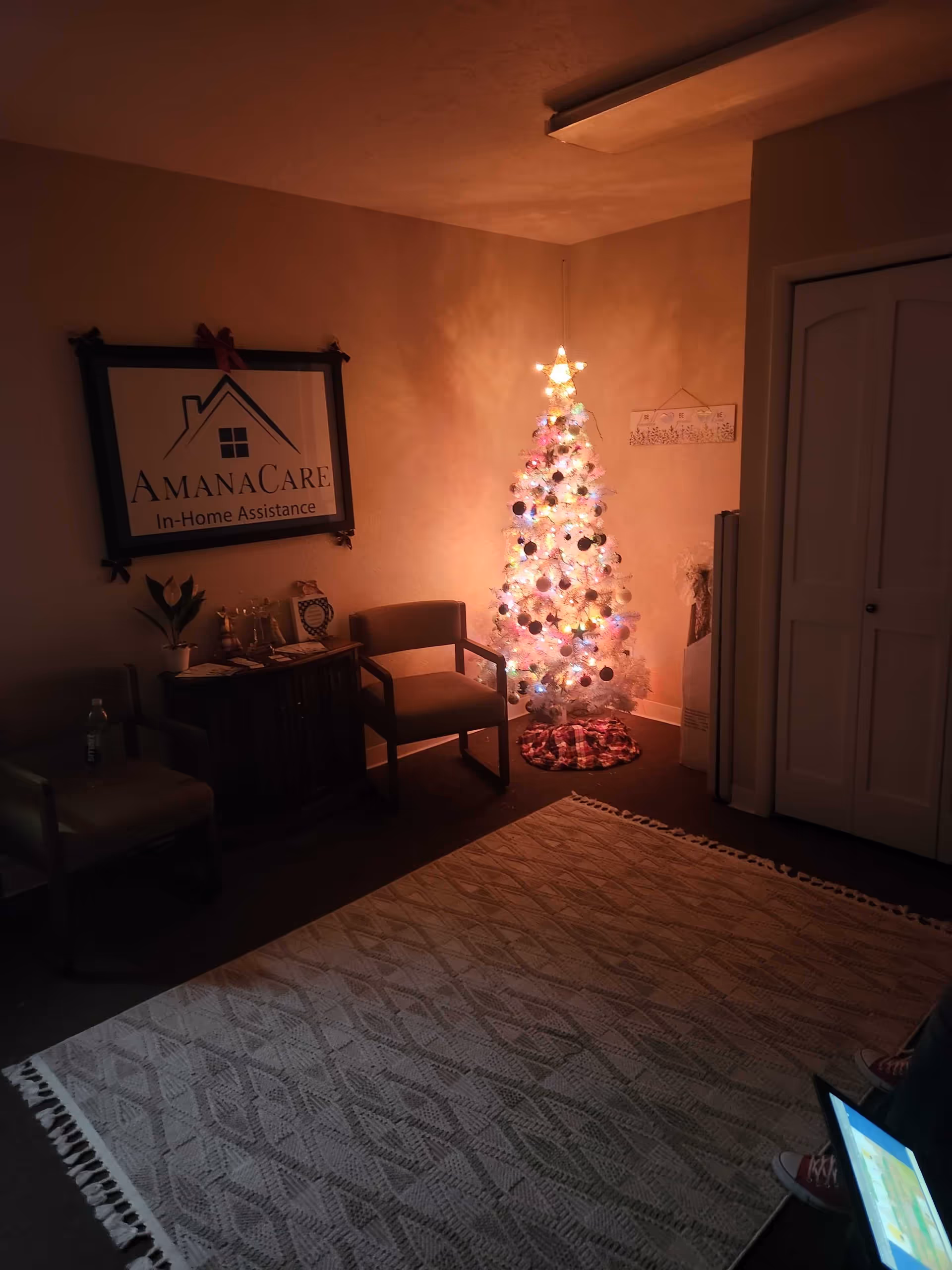 Dim indoor lobby with a lit Christmas tree and AmanaCare sign.