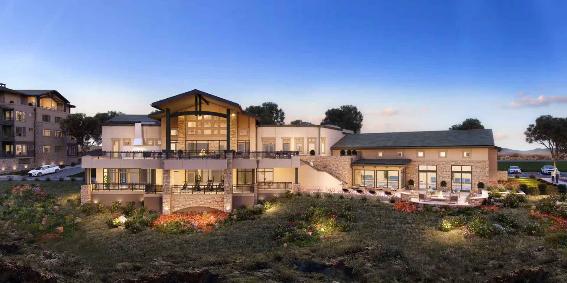 Exterior front view of a two-story senior living facility with landscaped grounds, outdoor seating patios, and illuminated windows at dusk.
