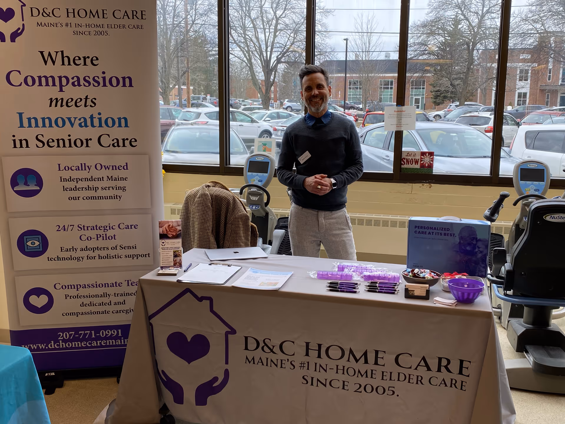Man stands beside D&C Home Care banner at an indoor promotional display.