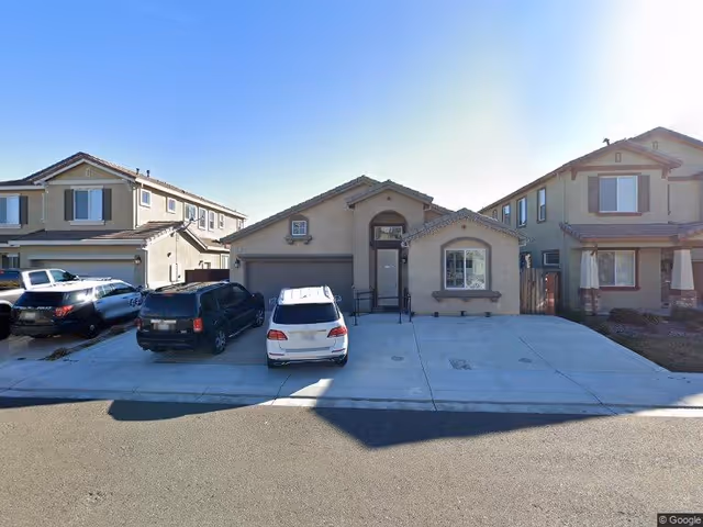 Front exterior of a single-story suburban house with a wide driveway and several cars parked in front.