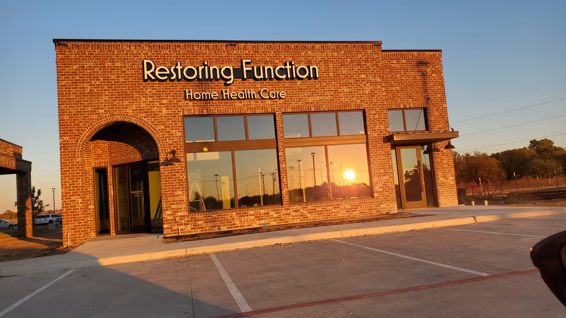 Brick building with Restoring Function Home Health Care sign and large windows at sunset.