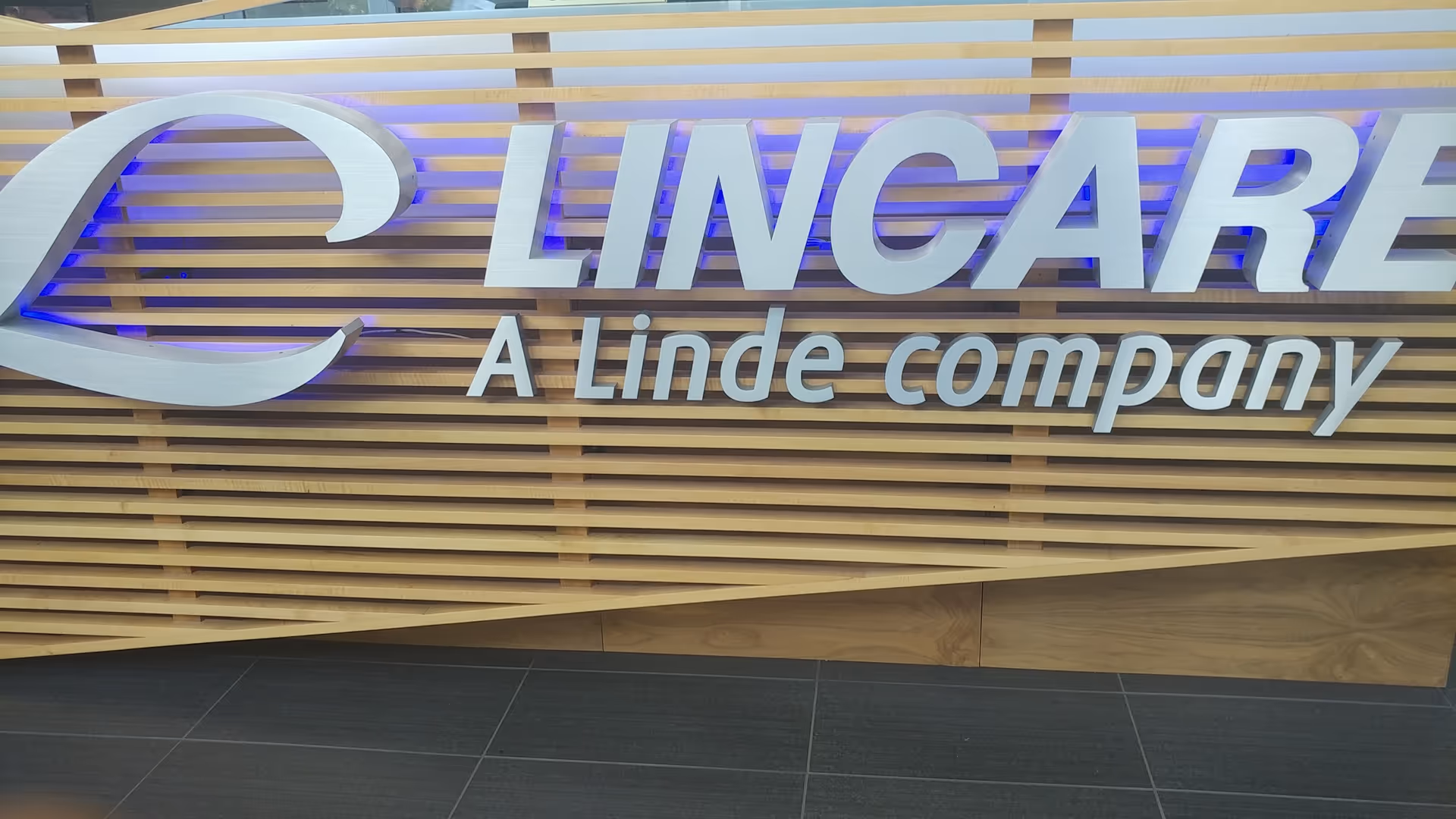 LINCARE sign mounted on a wooden slat wall inside a lobby.