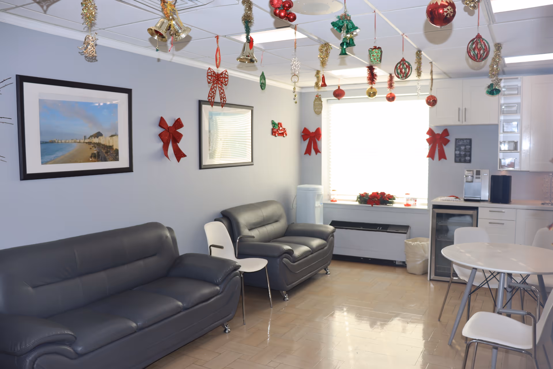 A holiday-decorated resident lounge with gray leather sofas, white chairs, and a kitchenette.
