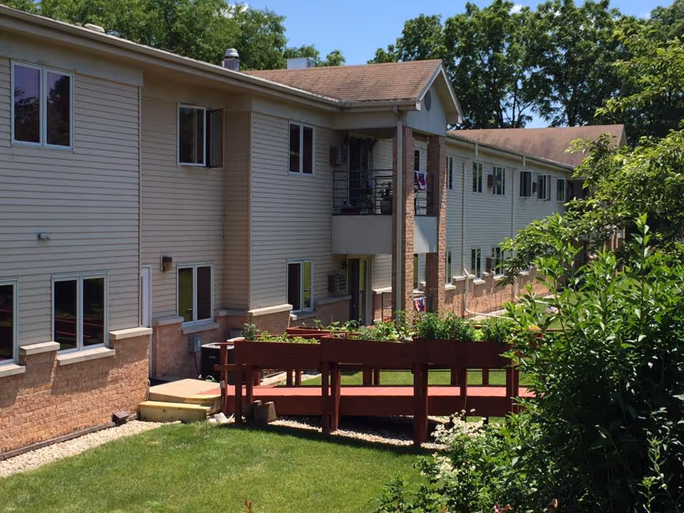 Exterior view of Trinity Pines Retirement Center with beige siding, brick base, and a red deck.